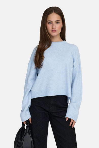 Pull col rond bleu de ONLY®, porté avec un pantalon noir taille haute et un sac assorti.
