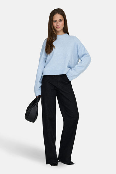 Pull col rond bleu de ONLY, porté avec un pantalon noir ample et un sac à main noir.