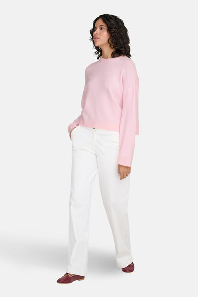 Ronde hals roze trui van ONLY®, gedragen met een witte broek en bordeauxrode platte schoenen.
