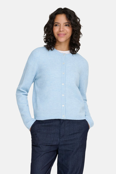 Cardigan bleu clair de ONLY, porté avec un pantalon foncé, avec les mains dans les poches.