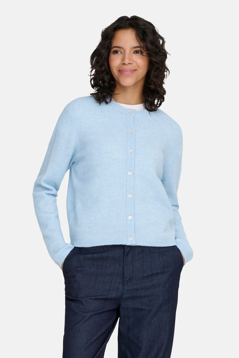 Cardigan bleu clair de ONLY, porté avec un pantalon foncé, avec les mains dans les poches.