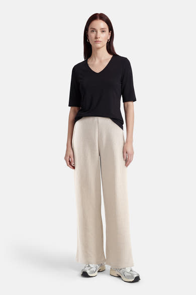 Pantalon écru de ONLY®, ample et texturé, porté avec un t-shirt noir à col en V et des chaussures de sport argentées.
