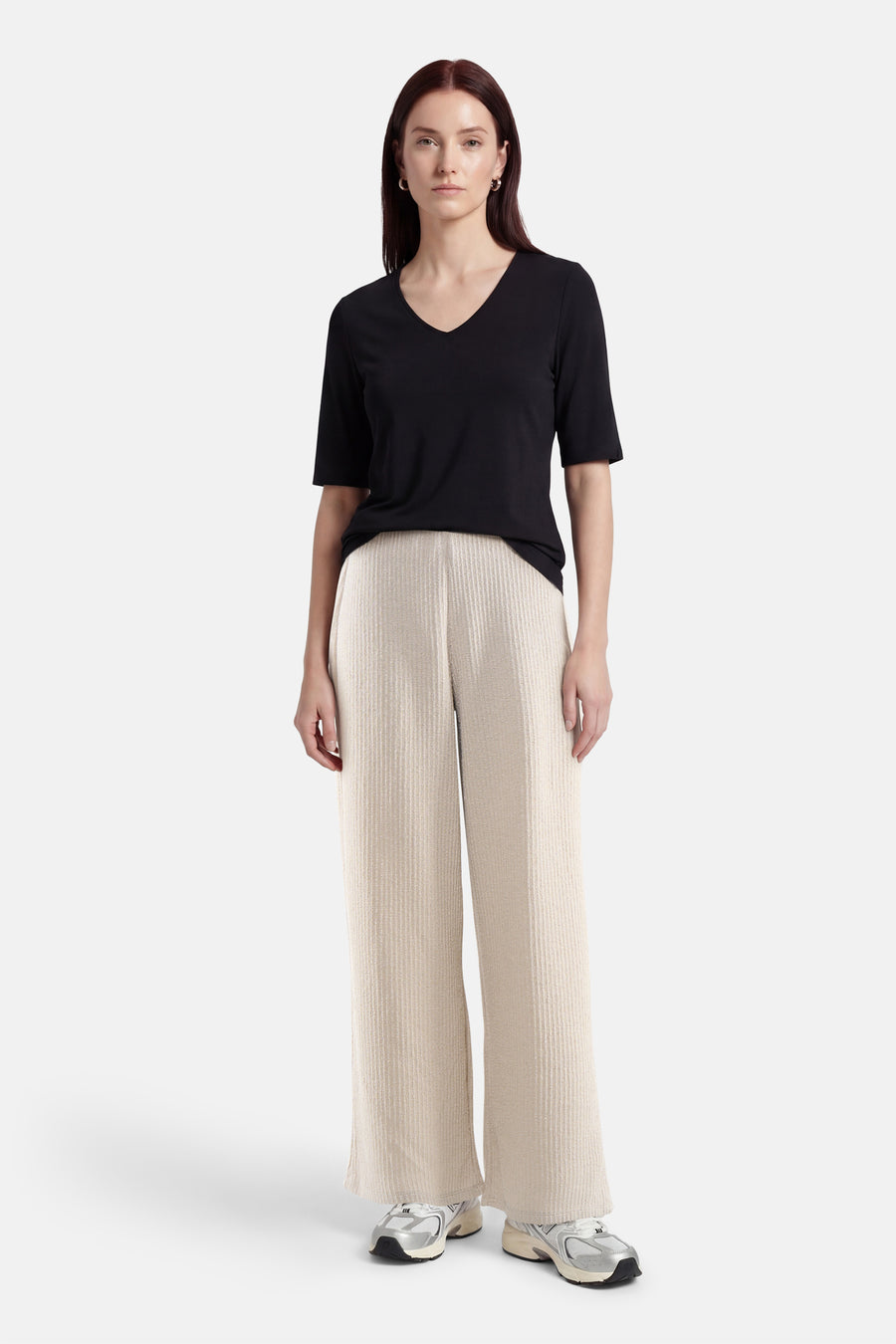 Pantalon écru de ONLY®, ample et texturé, porté avec un t-shirt noir à col en V et des chaussures de sport argentées.
