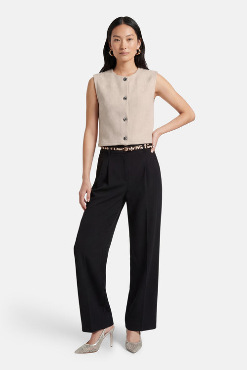 Gilet beige de ONLY®, boutonné, porté avec une ceinture à motif animalier, un pantalon noir taille haute et des escarpins argentés.
