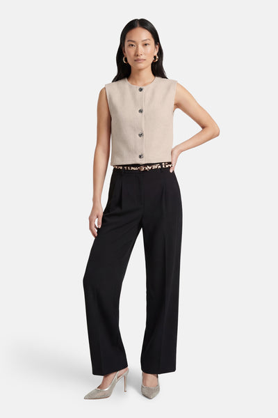 Gilet beige de ONLY®, boutonné, porté avec une ceinture à motif animalier, un pantalon noir taille haute et des escarpins argentés.
