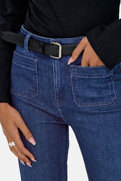 Donkerblauwe flared jeans van ONLY®, met opgestikte zakken, gedragen met een zwarte trui en een leren riem.