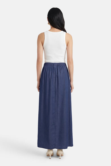 Lange spijkerrok in donkerblauw van JDY, met elastische tailleband, gedragen met een witte tanktop.