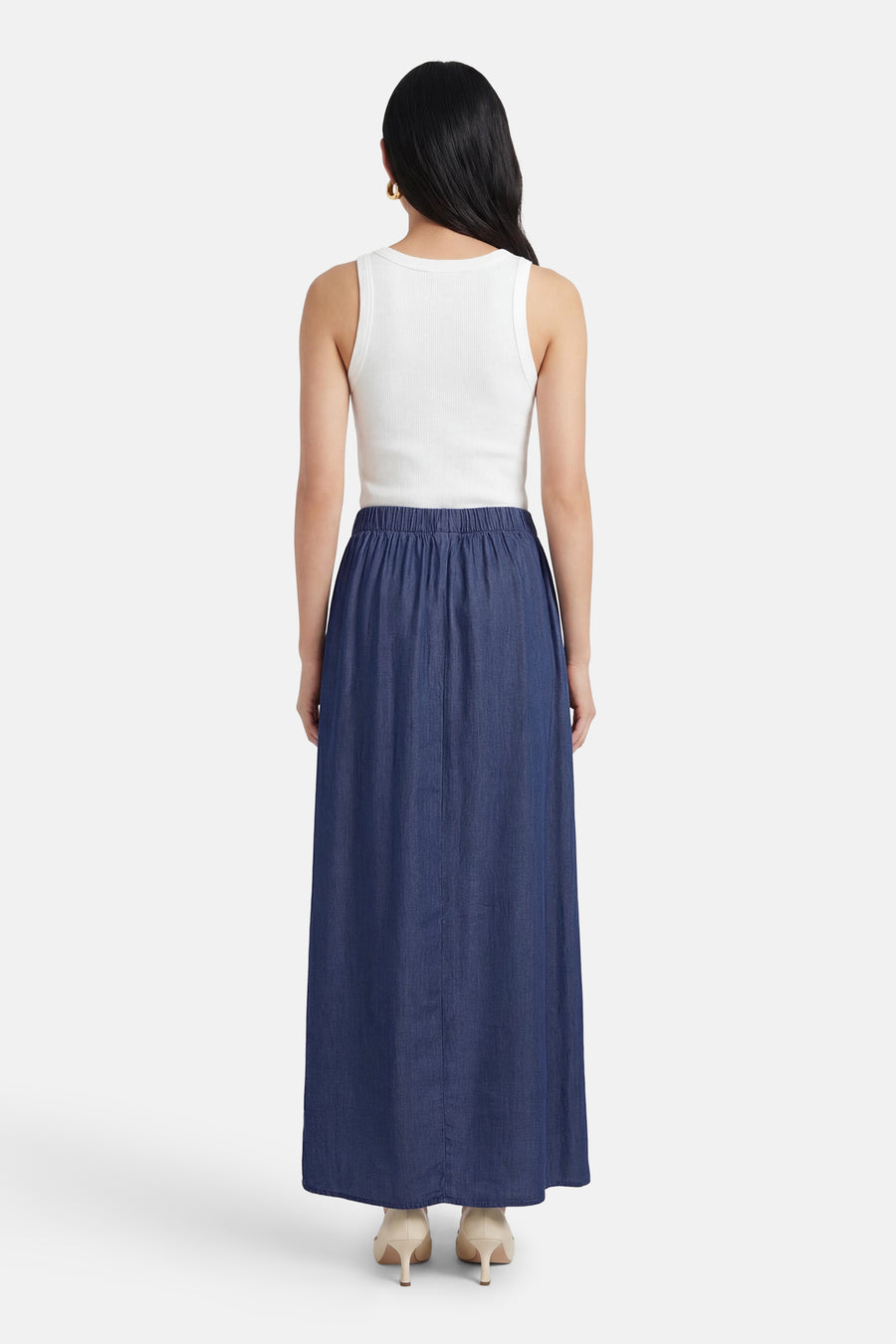 Lange spijkerrok in donkerblauw van JDY, met elastische tailleband, gedragen met een witte tanktop.