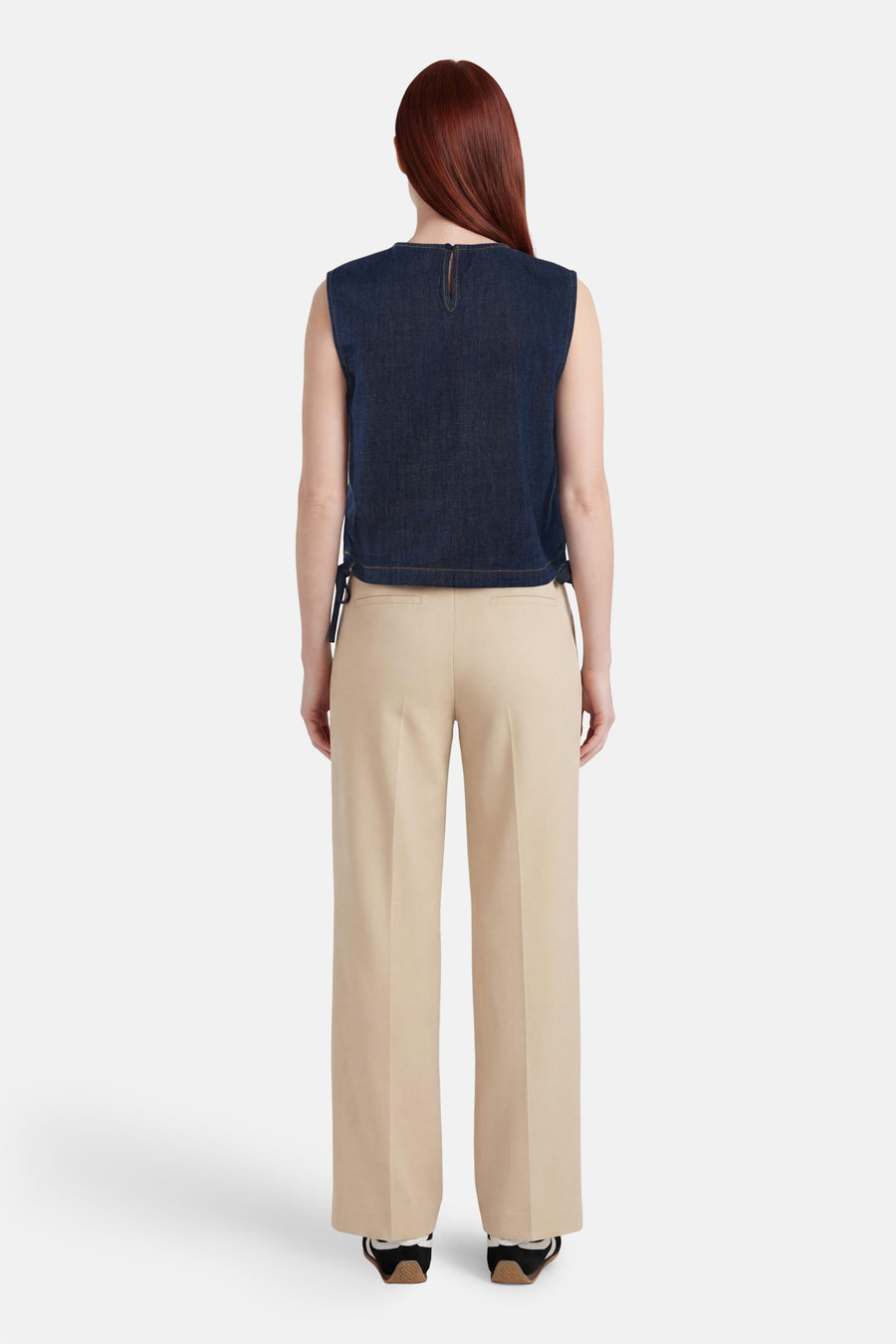 Top sans manches en jean bleu foncé d'ONLY, vue de dos, avec découpe goutte d'eau et liens latéraux, porté avec un pantalon beige et des baskets.