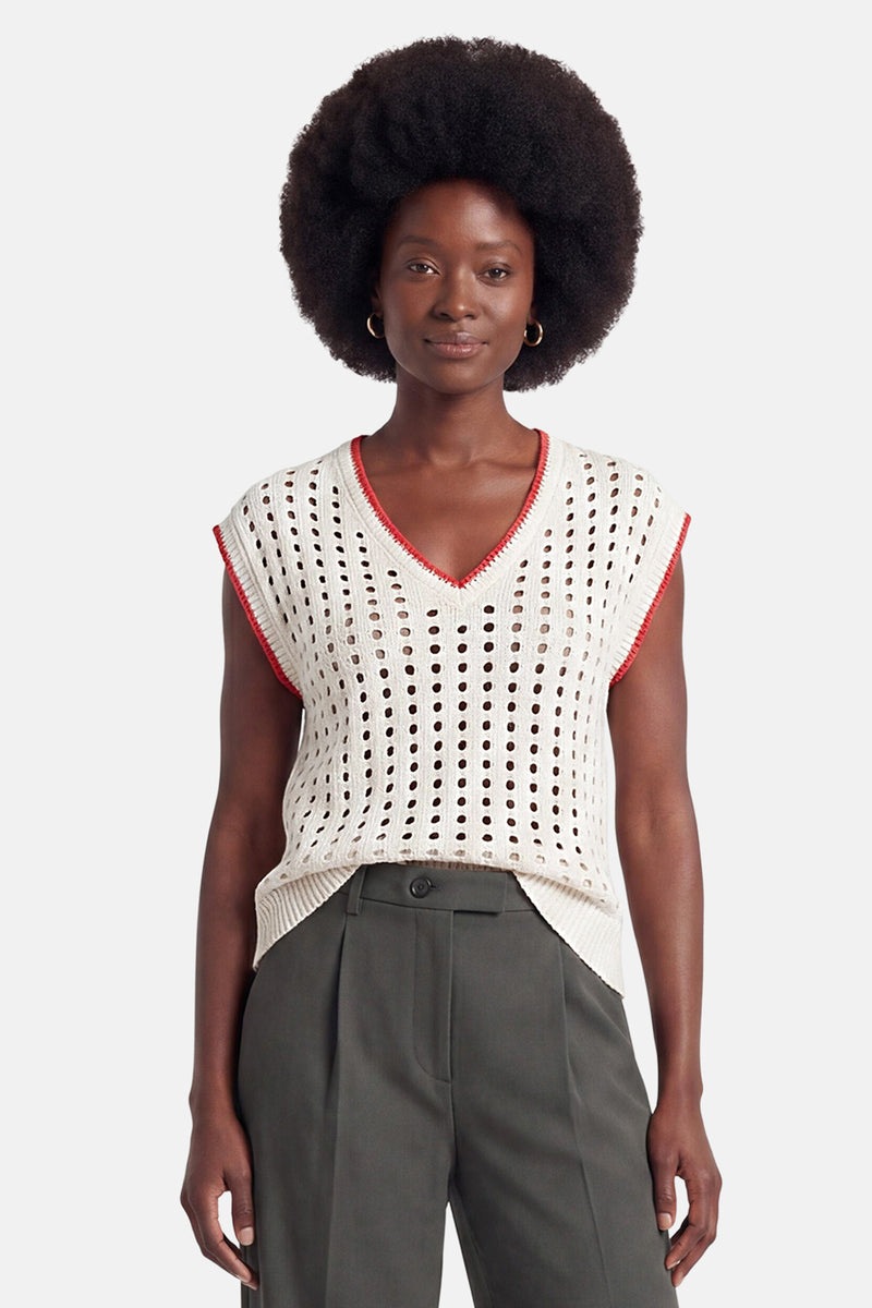Cream perforated knit sleeveless top with red trim, V-neck, and ribbed hem, worn with olive trousers, front view.