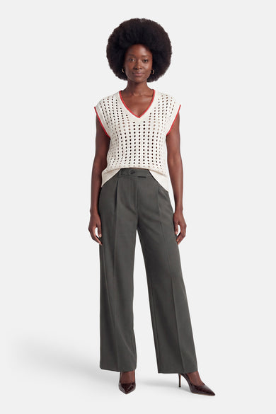 Cream perforated knit sleeveless debardeur with red trim, worn with olive wide-leg trousers and brown pointed heels, front view.