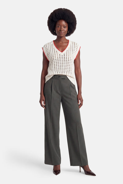 Cream perforated knit sleeveless debardeur with red trim, worn with olive wide-leg trousers and brown pointed heels, front view.
