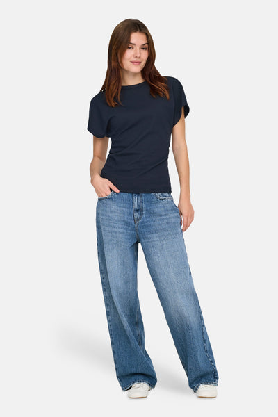 T-shirt bleu à manches courtes de ONLY, porté avec un jean ample et des chaussures de sport blanches.