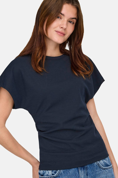 Blauw T-shirt met korte mouwen van ONLY, gedragen met een spijkerbroek en bruin golvend haar.