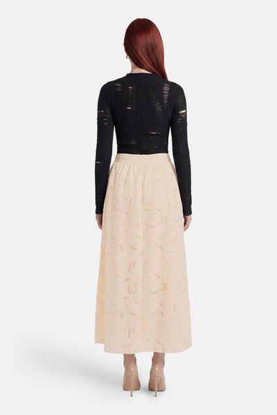 Beige long skirt with floral lace texture, back view, paired with black top and nude heels