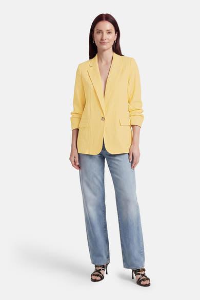 Blazer jaune de ONLY® avec manches retroussées, un bouton, poches et porté avec un jean et des talons noirs.