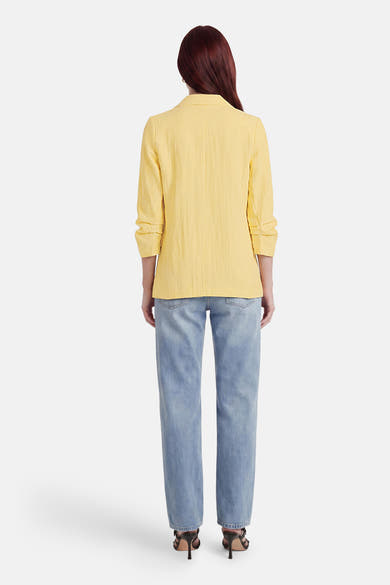 Blazer jaune de ONLY® avec manches retroussées, porté de dos sur un jean et des sandales à talons.