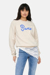 Sweat-shirt beige ONLY orné du mot « Paris » en bleu, porté avec un jean et un jupon en dentelle.
