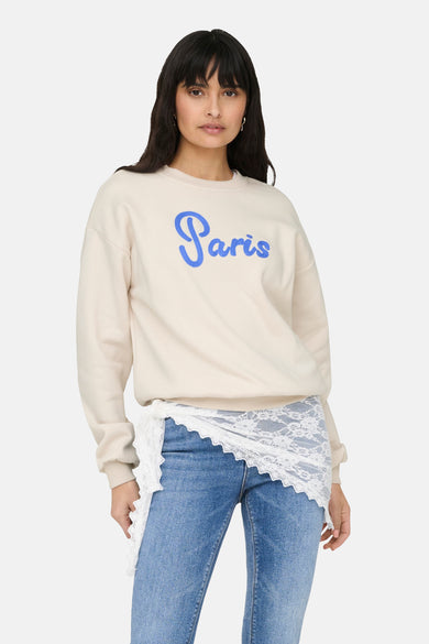 Beige rondehals sweatshirt van ONLY®, gedragen met een blauwe jeans en lichte hakken.