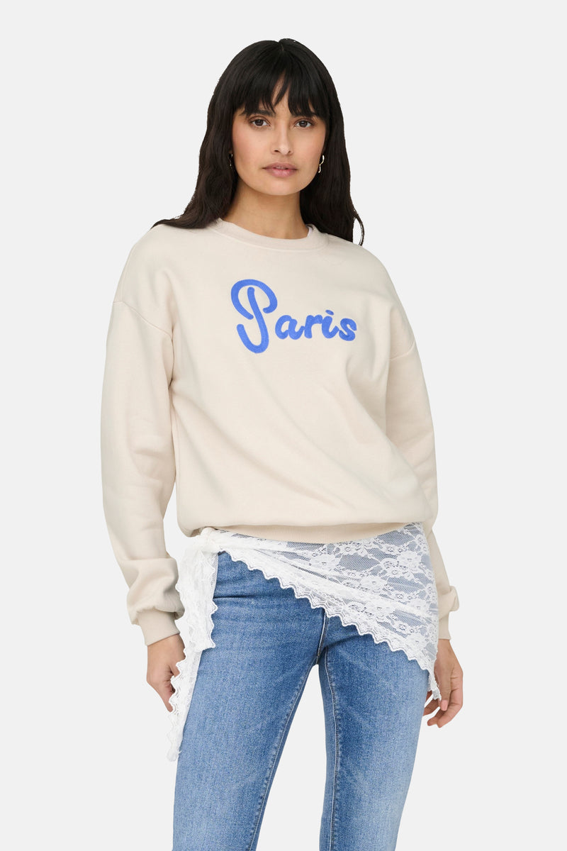 Beige rondehals sweatshirt van ONLY®, gedragen met een blauwe jeans en lichte hakken.