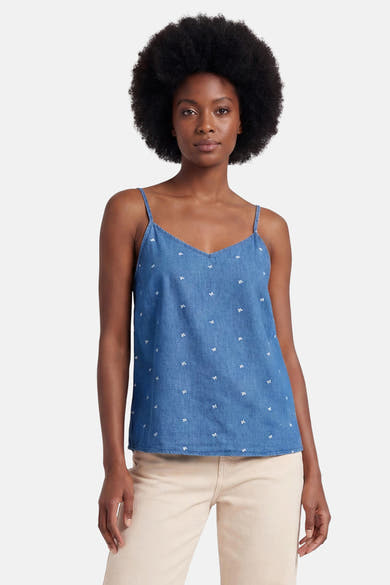 Débardeur en jean bleu moyen de ONLY® à motifs de petits nœuds blancs, col en V et fines bretelles, porté sur un pantalon beige.