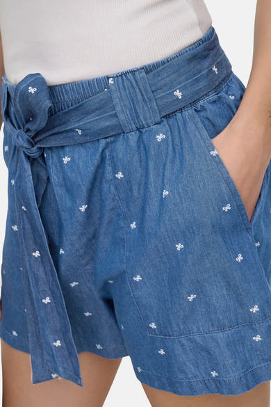 Korte spijkerbroek in middellichte denim van ONLY® met wit knoopmotief, elastische tailleband en strikceintuur, één hand in de zak.