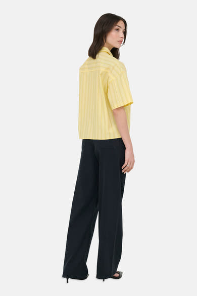 Chemise à manches courtes jaune de JDY à fines rayures verticales, portée de dos avec un pantalon ample noir.
