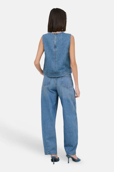 Mouwloos spijkerblouse in lichtblauw van JDY, achterkant met ritssluiting. Gedragen met een wijde spijkerbroek en muiltjes met hak.