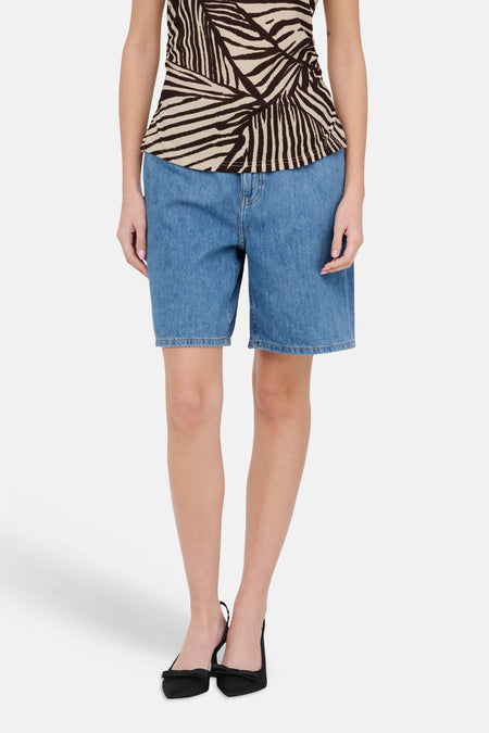 Short en jean bleu clair de JDY, long, porté avec un top zébré marron et beige et des escarpins noirs.