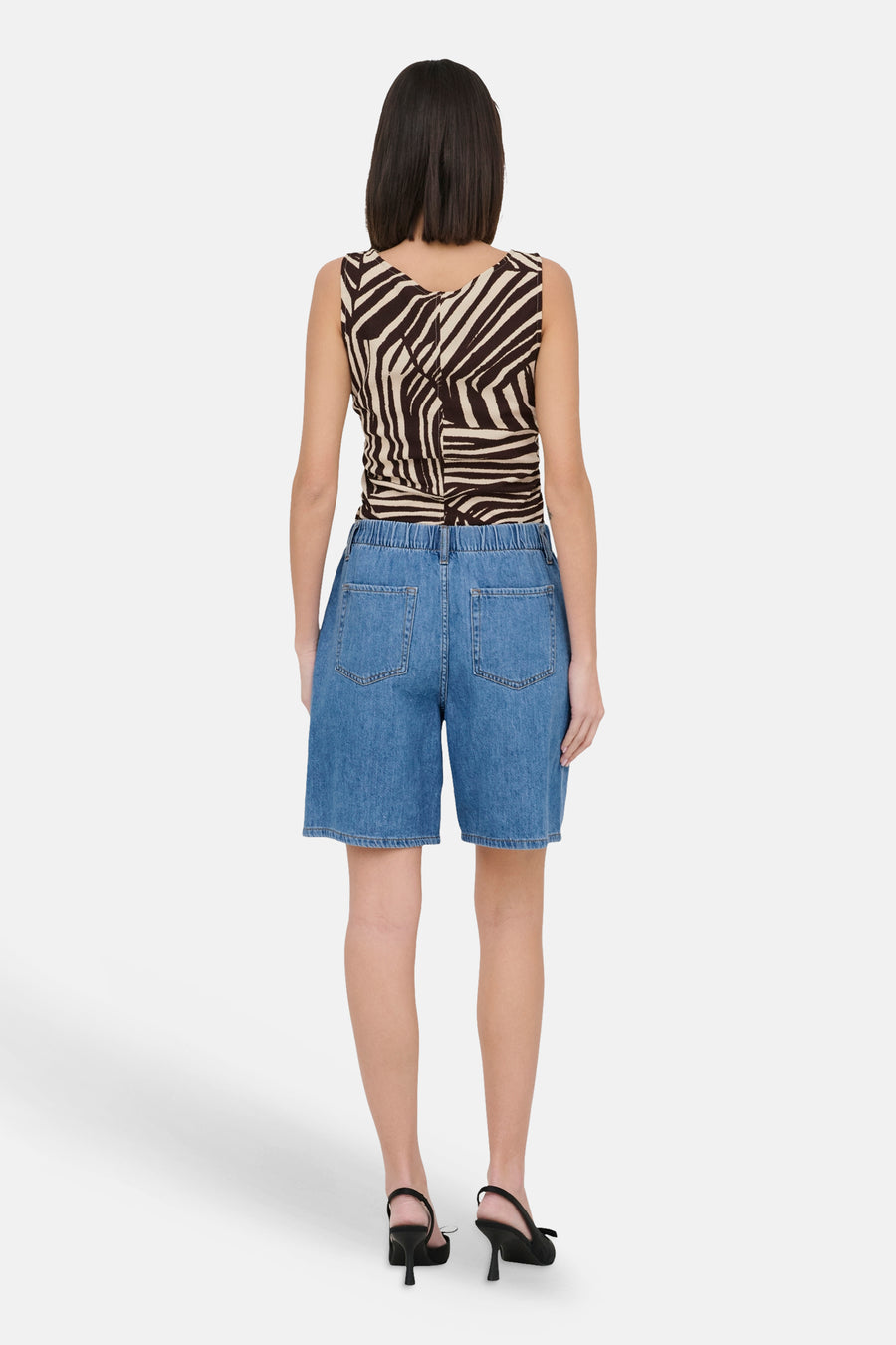 Lichtblauwe spijkerbroekshorts van JDY, achterkant, met elastische tailleband en achterzakken, gedragen met een gestreept hemdje.