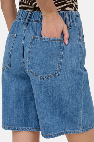 Lichtblauwe spijkerbroekshorts van JDY, achterkant, elastische tailleband, opgestikte zakken en hand in de zak, gedragen met een gestreept topje.