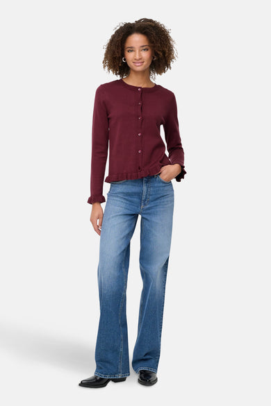 Cardigan bordeaux en maille by ONLY, avec boutons et finitions volantées, porté avec un jean et des chaussures noires.
