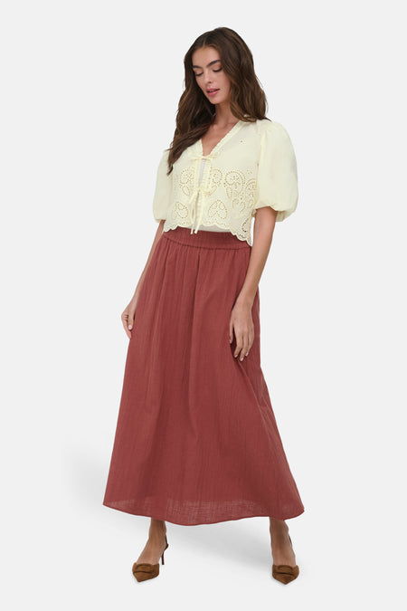 Chemise jaune de ONLY à broderie anglaise et cœurs, liens à nouer sur le devant, manches bouffantes, portée avec une jupe longue rouille.