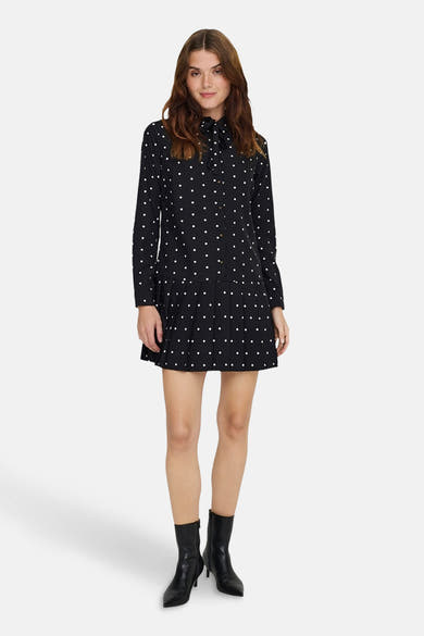 Robe noire à pois blancs de ONLY, avec col à nouer et ourlet plissé, portée avec des bottines en cuir noires.
