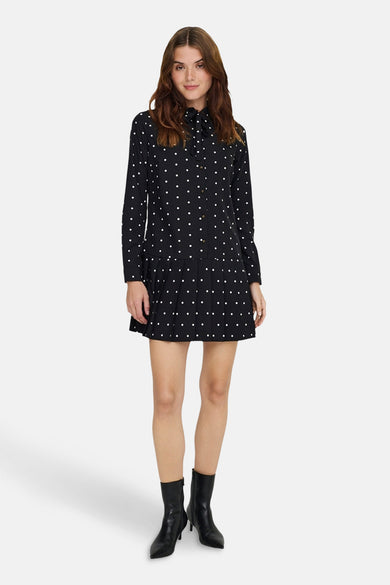 Robe noire à pois blancs de ONLY, avec col à nouer et ourlet plissé, portée avec des bottines en cuir noires.

