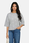 Grijze sweater met bloemenprint van ONLY, gedragen met een wijde blauwe jeans en een crèmekleurige handtas.