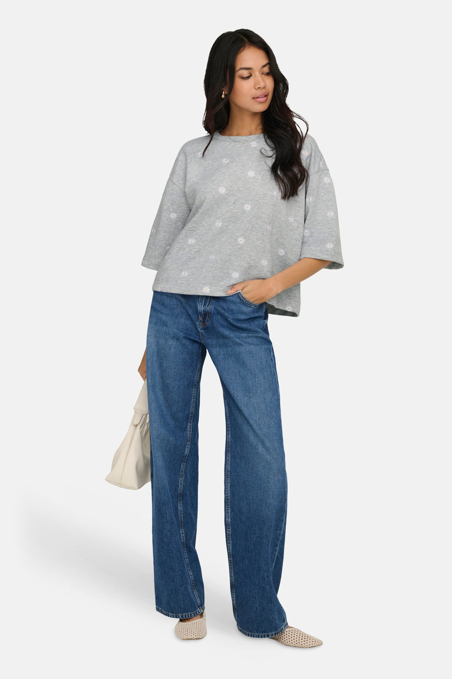Sweat-shirt gris à fleurs de ONLY, porté avec un jean bleu ample et un sac à main crème.