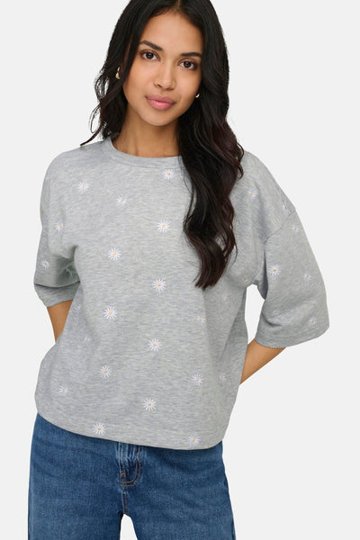 Gemêleerd grijs sweatshirt van ONLY, met geborduurd bloemenpatroon, gedragen met een spijkerbroek.