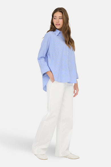 Chemise à manches longues bleue rayée de ONLY®, portée avec un pantalon blanc large.