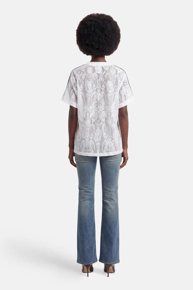 Vue de dos d'un T-shirt blanc en dentelle de ONLY® à manches courtes avec rayures noires aux épaules et motif élaboré, porté avec un jean et des talons.
