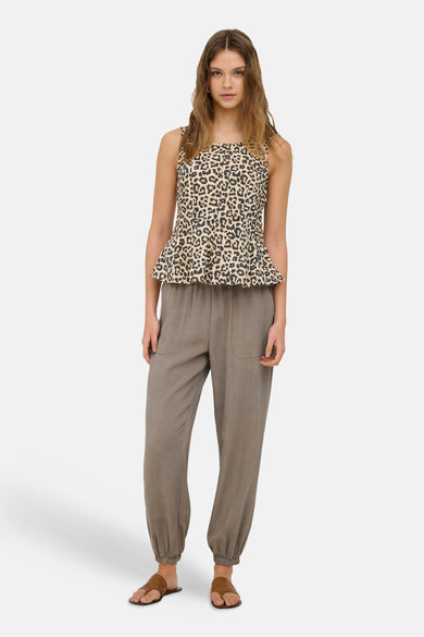 Sleeveless leopard-print blouse in pumice stone, featuring a peplum hem and square neckline, worn with relaxed-fit trousers and brown sandals.