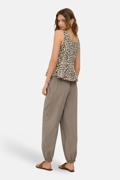 Sleeveless leopard-print blouse in beige and black, featuring a peplum hem, shown from back view on model wearing taupe pants and sandals.