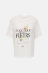 T-shirt blanc de JDY avec imprimé floral et texte français "La Boutique de Fleurs" sur le devant.