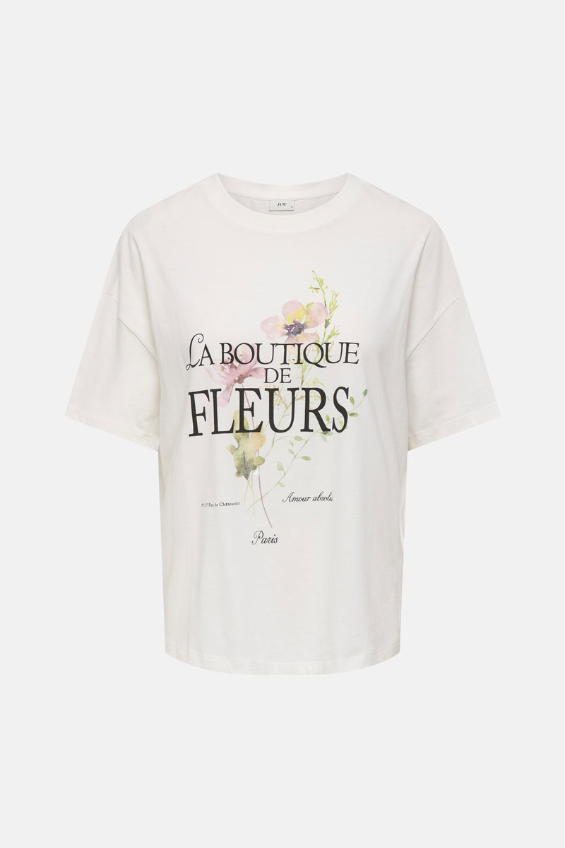 T-shirt blanc de JDY avec imprimé floral et texte français "La Boutique de Fleurs" sur le devant.