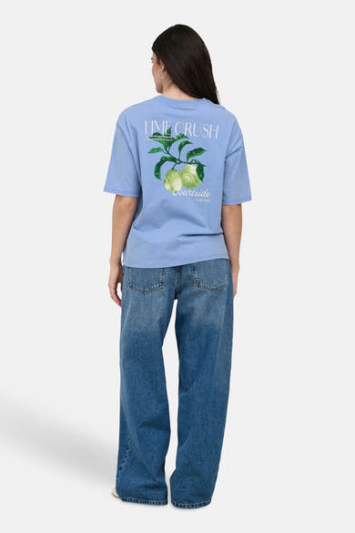 T-shirt bleu à manches courtes de ONLY® avec motif "LIME CRUSH" et citrons verts au dos, porté avec un jean ample, vue de dos.