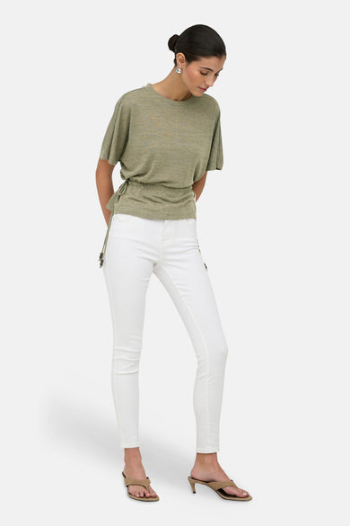 Pull kaki de ONLY avec cordons de serrage perlés sur le côté, porté avec un jean blanc et des sandales à talons.