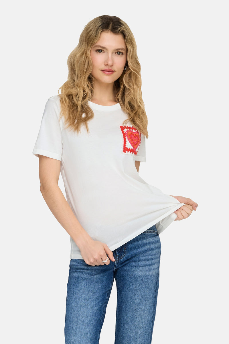 Wit T-shirt met korte mouwen van ONLY, versierd met een rood gehaakt hart, gedragen met een blauwe jeans en rode ballerina's.
