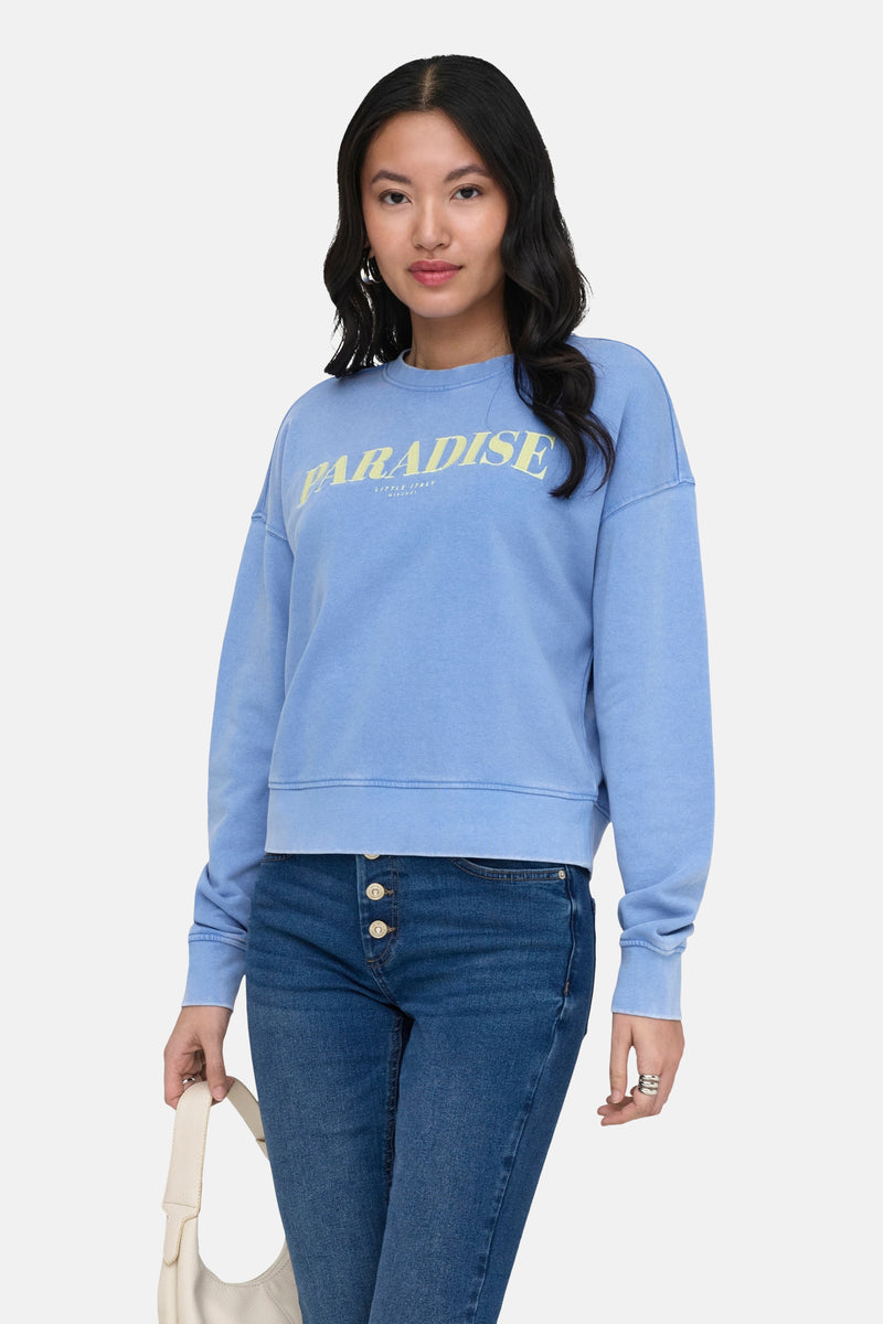 Sweat col O bleu délavé de ONLY® avec inscription 'PARADISE' jaune, porté sur un jean.