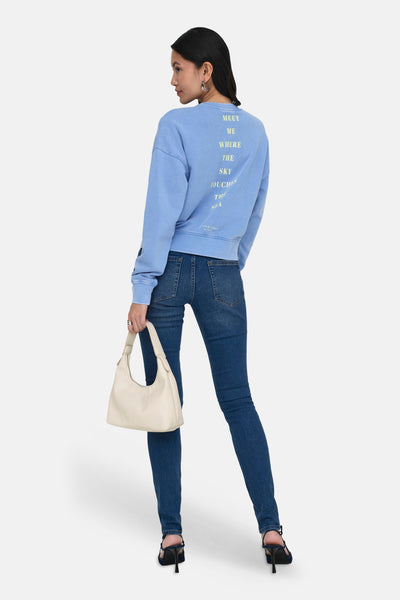 Sweat col O bleu de ONLY® avec texte au dos, porté de dos avec un jean et un sac à main crème.