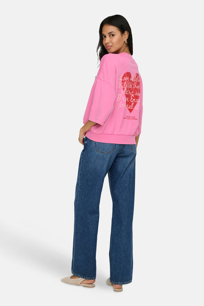 Roze ONLY sweatshirt met hartprint en bedrukte letters op de rug, gedragen met een blauwe jeans.